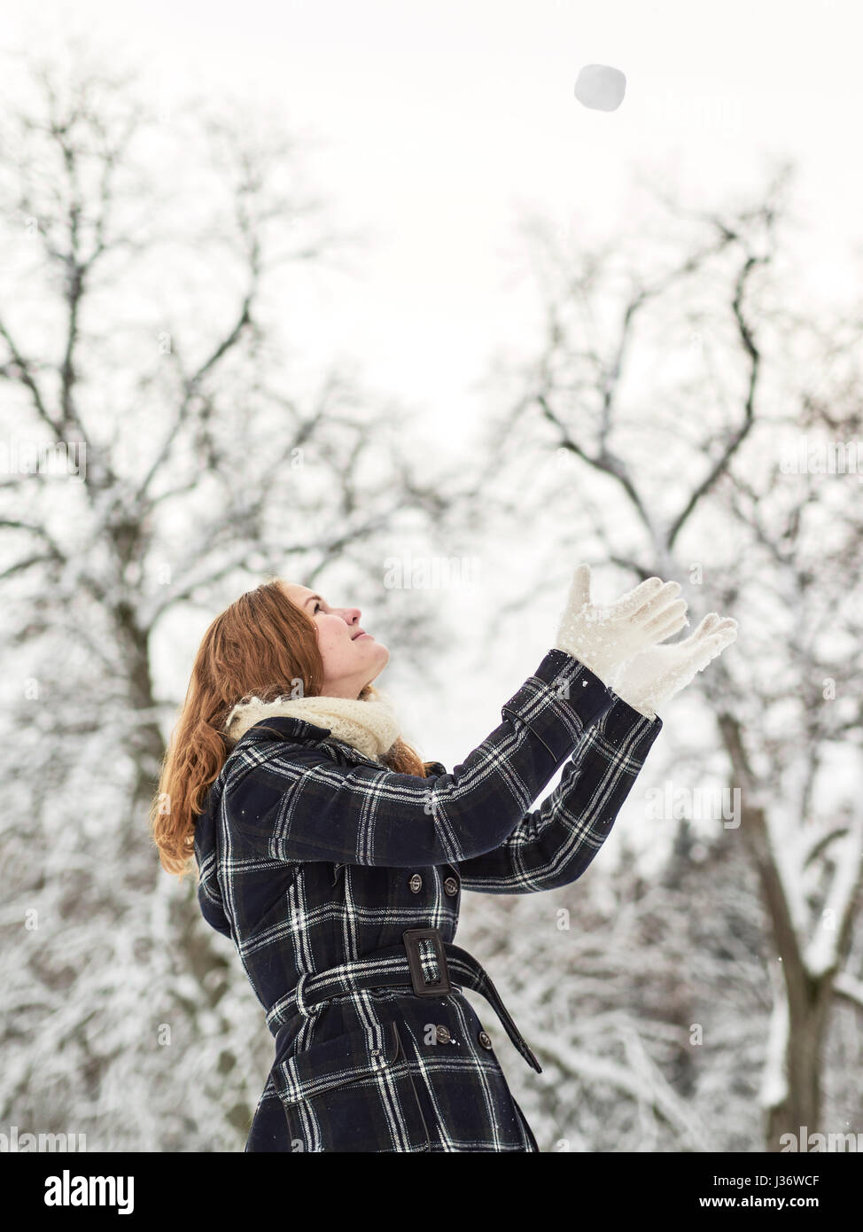 Schöne junge Mädchen tragen einen Wintermantel und werfen Schneeball in der Luft, Finnisch Wintertag im Februar Stockfoto