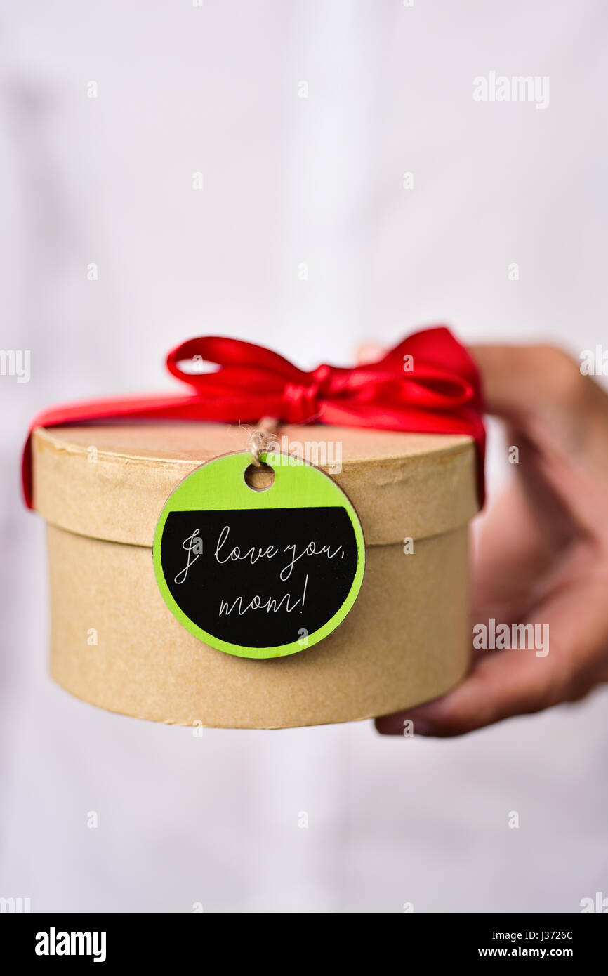 Nahaufnahme eines jungen kaukasischen Mann in einem weißen Hemd mit Geschenk-Box mit einem roten Band und mit einem grünen und schwarzen Etikett verbunden mit dem Text an sie gebunden. Stockfoto