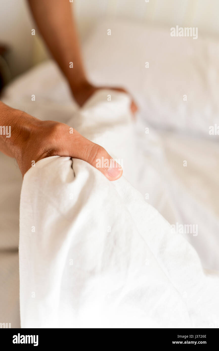 Nahaufnahme eines jungen Mannes erweitern die Bettlaken oder der Bettdecke auf der Matratze, wie er das Bett macht Stockfoto