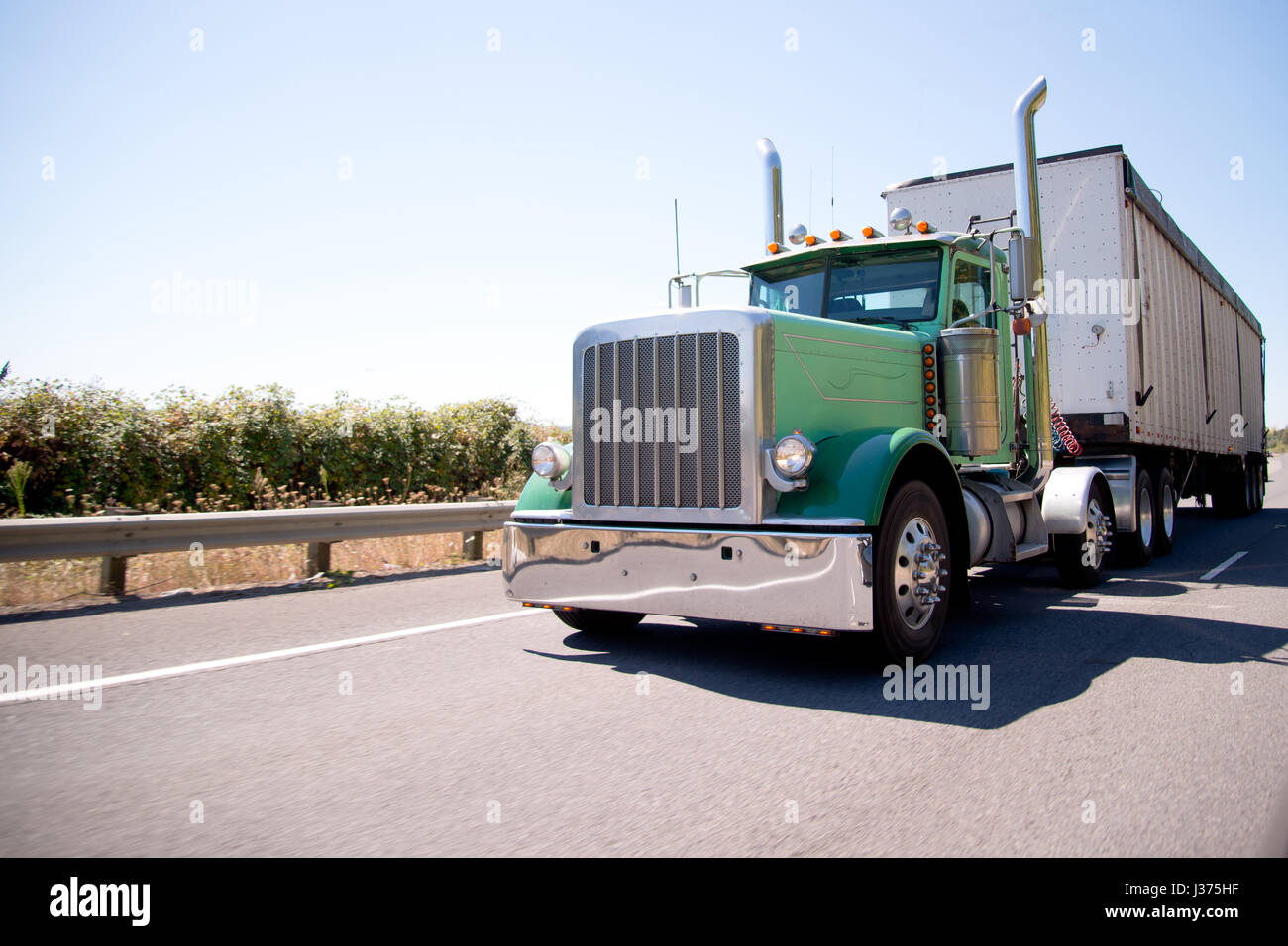 Klassische amerikanische bonneted große grüne rig Semi Truck mit hohen elegante verchromte Auspuffrohre Transport von kommerziellen Ladung in Bulk Container Anhänger Stockfoto