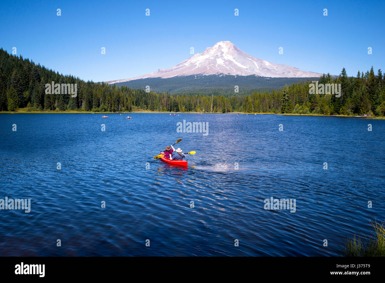 Paar tragen Hüte aktive Erholung im Freien auf der schönen Trillium Lake Recreation, Rudern auf dem roten Kayak in Richtung der hohen schneebedeckten Mount Hood Stockfoto