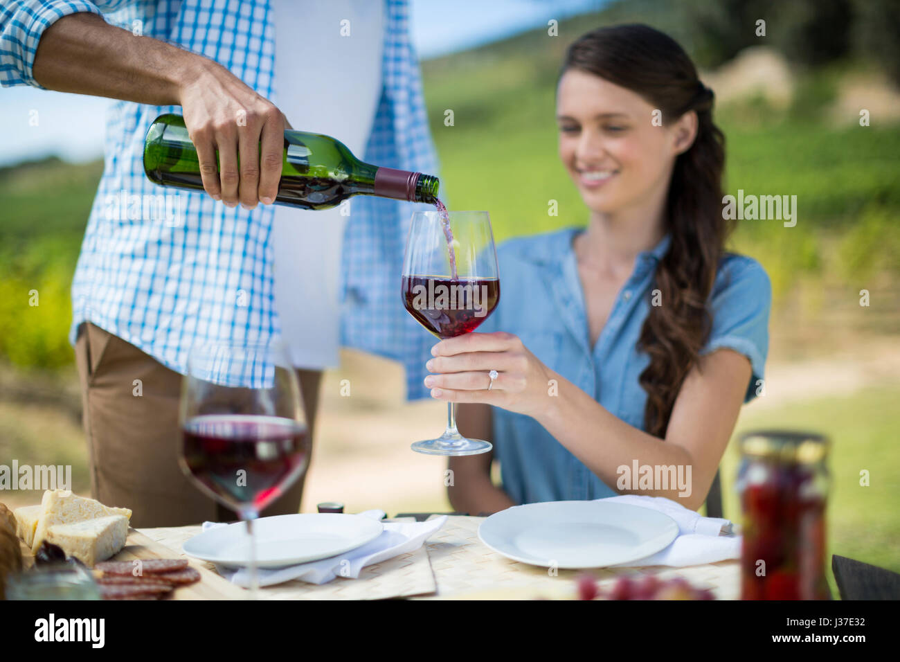 Man gießt Rotwein im Glas gehalten von Frau am Tisch sitzen Stockfoto
