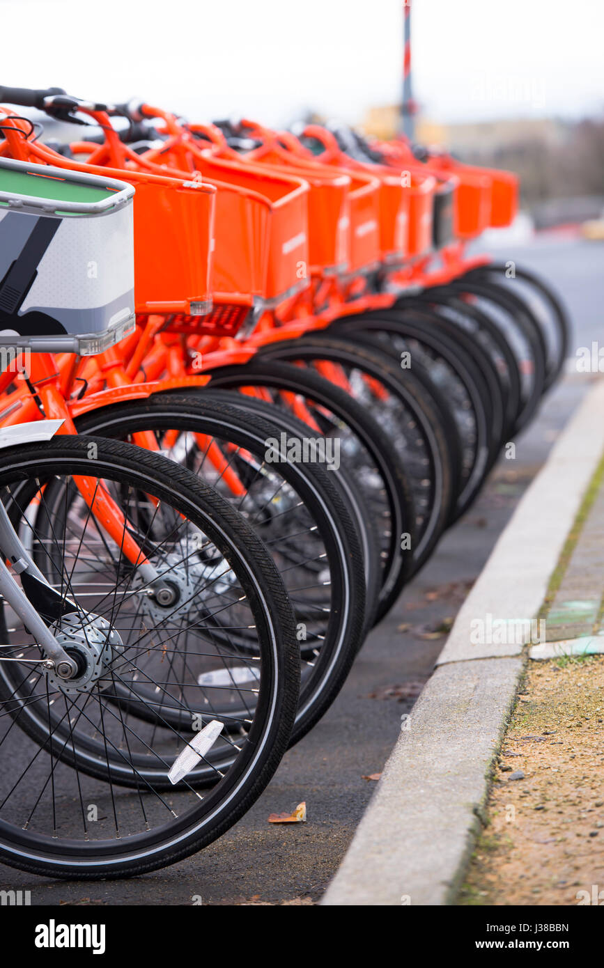 Orange Bikes mit Körben vor und polierten Räder für bezahlte öffentliche Nutzung bleiben gesäumt und einen grauen Bike symbolische nicht wahrscheinlich andere stand out Stockfoto