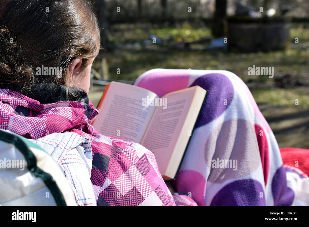 Junge Frau im Freien sitzen, bedeckt mit Decke und ein Buch zu lesen, an schönen Frühlingstag. Stockfoto