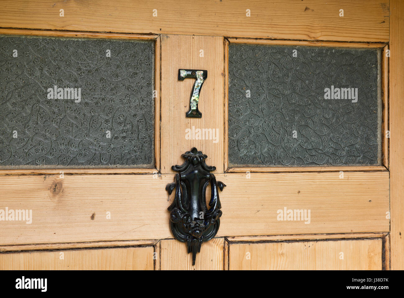 Die Zahl Sieben und ein Cast Türklopfer auf einem Verglasten verglasten, hölzerne Eingangstür eines uk Home. Stockfoto