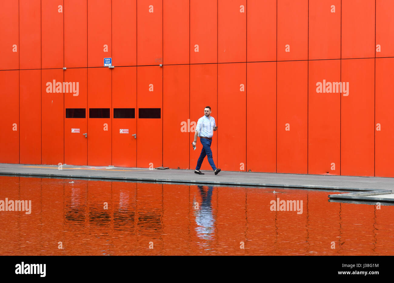 Mann mit roten Gebäude in der Backgroung reflektiert auf ein Wasser bei Fiera Rho Pero in Mailand. Stockfoto