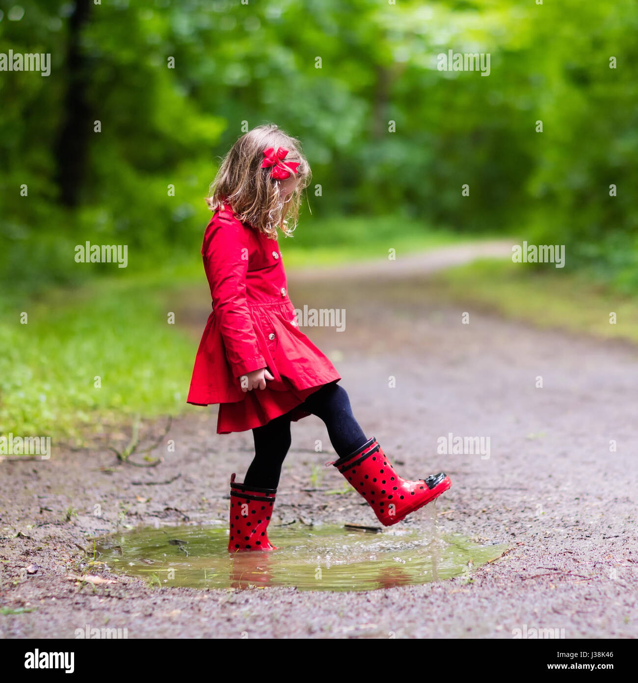 Kleines Mädchen im Regensommer Park spielen. Kind mit roten Marienkäfer-Regenschirm,  wasserdichte Jacke und Stiefel in Pfütze springen und im Regen Schlamm.  Kind walkin Stockfotografie - Alamy