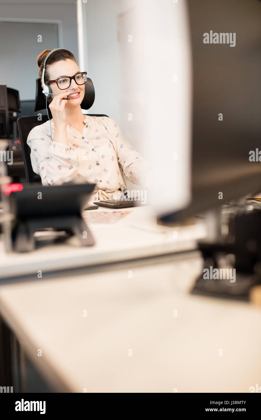 Lächeln, Geschäftsfrau, reden über Kopfhörer beim Sitzen im Büro Stockfoto