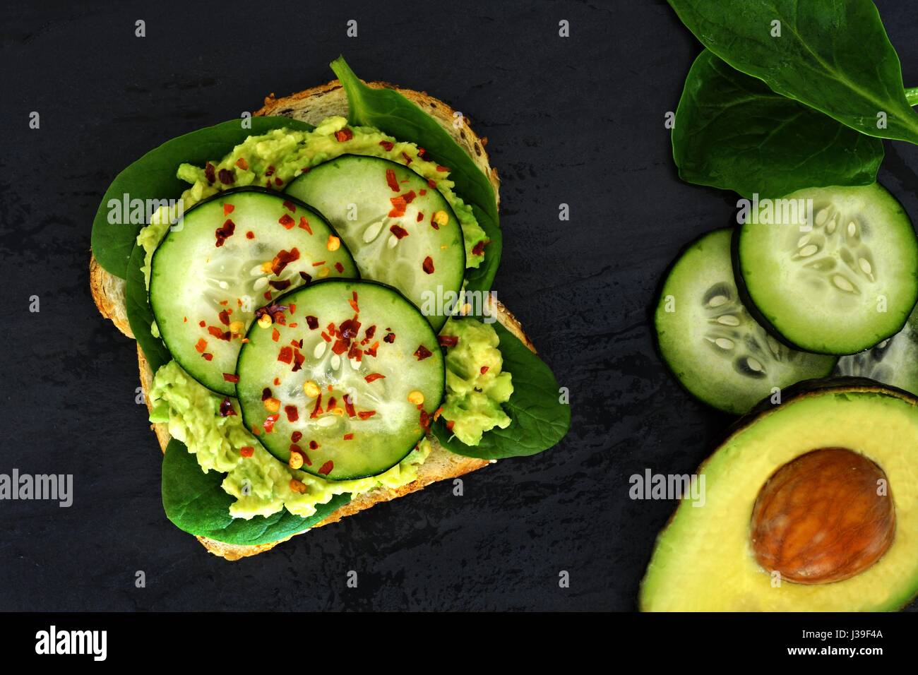 Offenen Avocado Sandwich mit Gurken und Spinat auf Vollkornbrot vor einem dunklen Hintergrund Schiefer Stockfoto