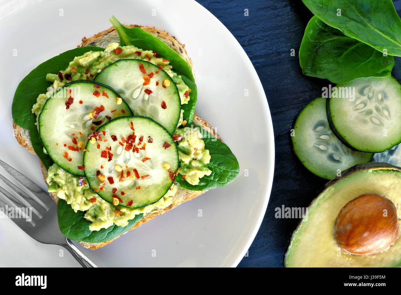 Avocado-Toast mit Gurke, Spinat und Vollkornbrot auf weißen Teller Schiefer im Hintergrund Stockfoto
