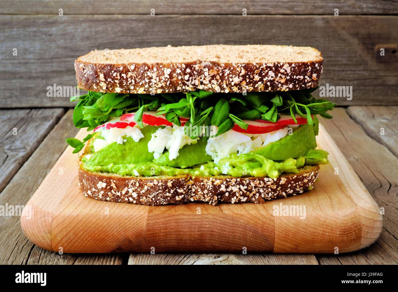 Superfood-Sandwich mit Avocado, Eiweiß, Radieschen und Erbsen schießt auf Vollkornbrot vor einem rustikalen Holz Hintergrund Stockfoto