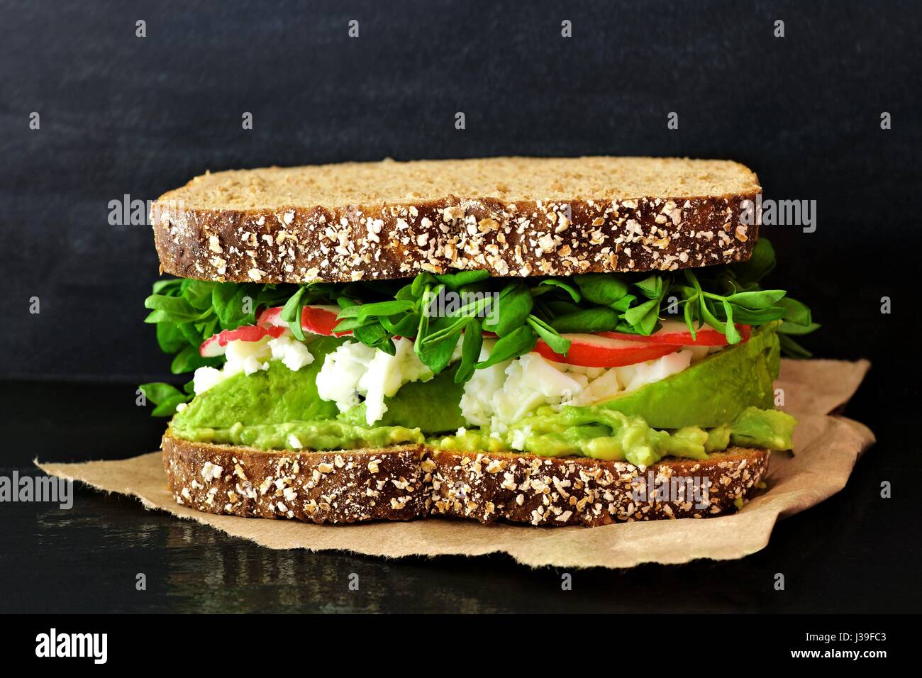 Superfood-Sandwich mit Avocado, Eiweiß, Radieschen und Erbsen schießt auf Vollkornbrot Schiefer im Hintergrund Stockfoto