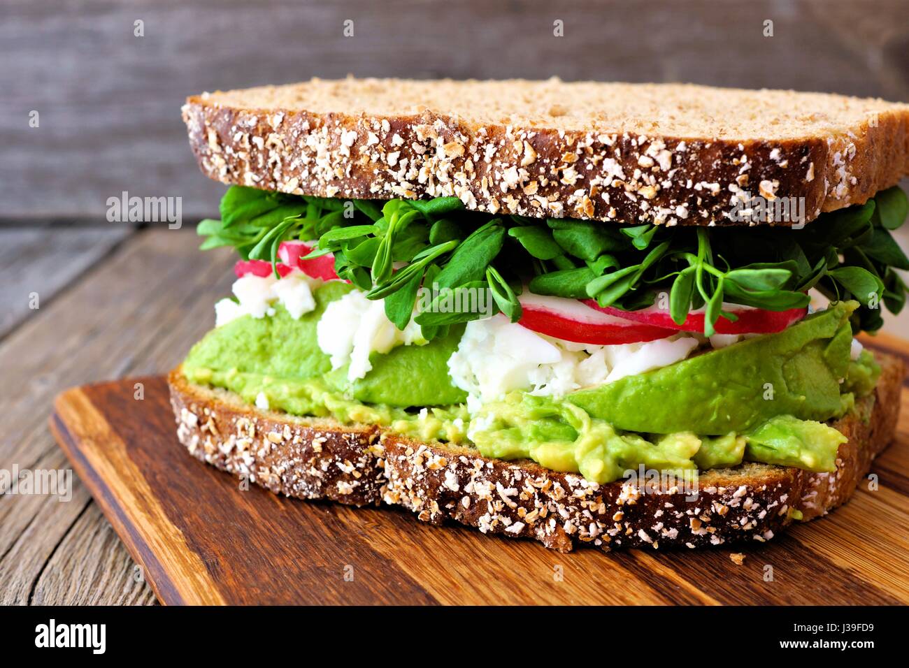 Superfood-Sandwich mit Vollkornbrot, Avocado, Eiweiß, Radieschen und Erbsen schießt auf Holzplatte Stockfoto