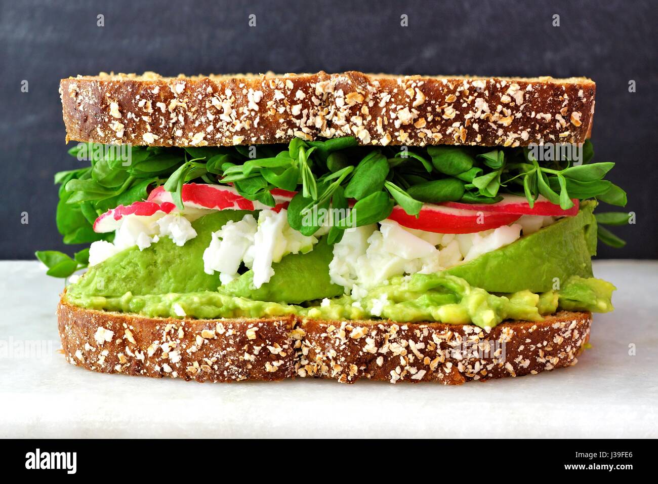 Superfood-Sandwich mit Vollkornbrot, Avocado, Eiweiß, Radieschen und Erbsen schießt auf Marmor vor schwarzem Hintergrund Stockfoto