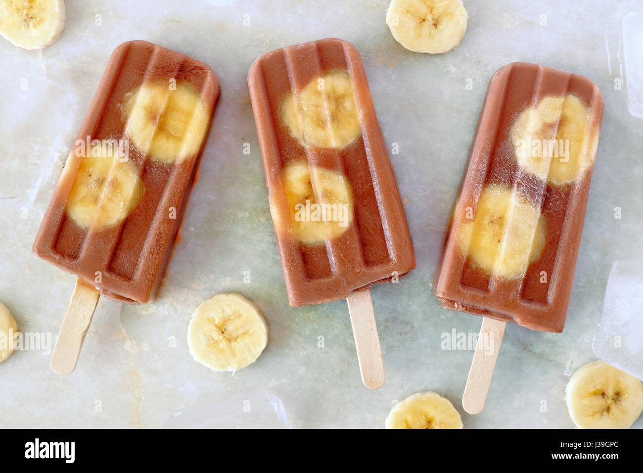 Schoko-Bananen Eis am Stiel mit in Scheiben geschnittenen Bananen auf weißem Marmor Hintergrund Stockfoto