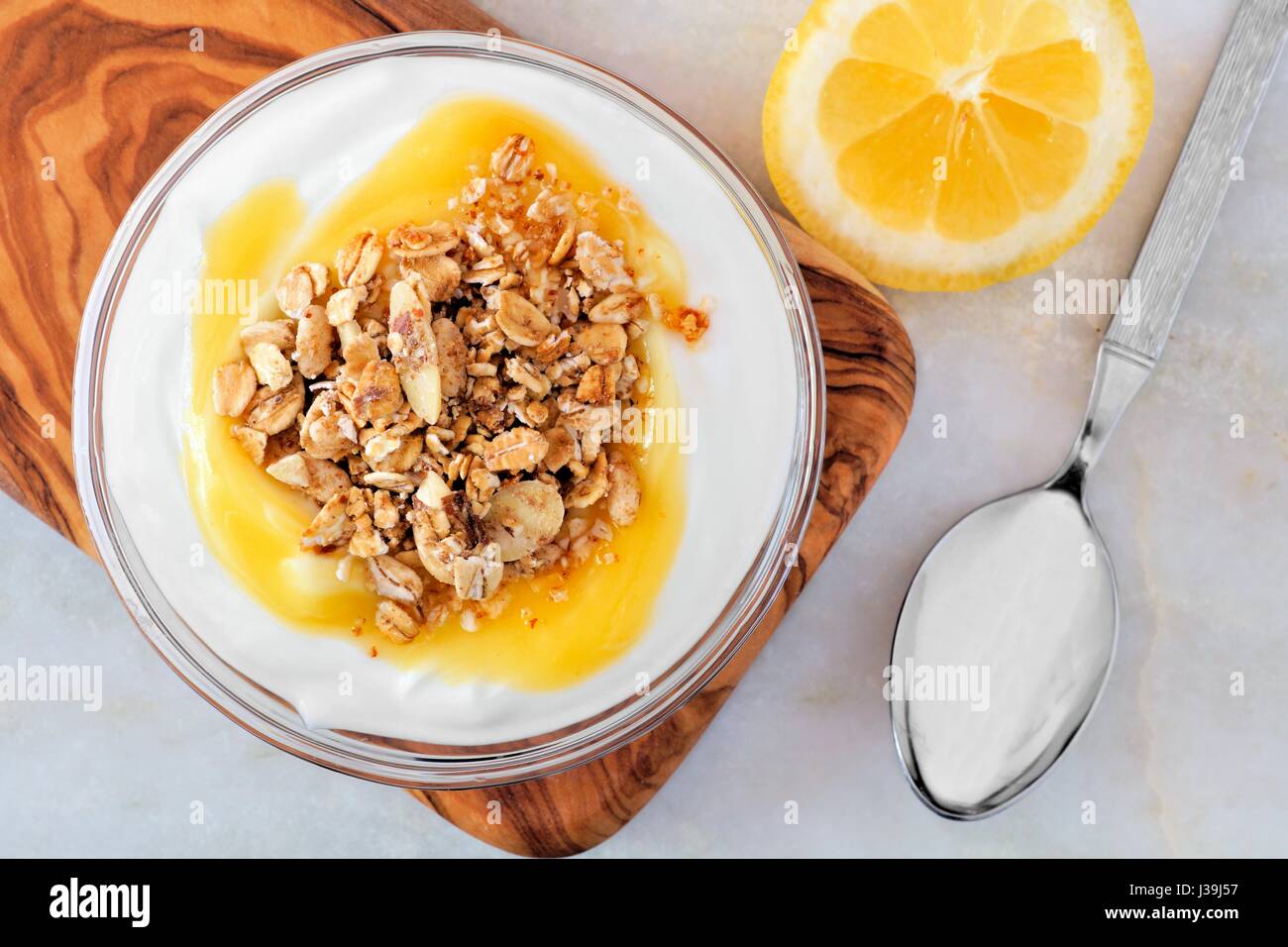 Schale der Zitrone aromatisierter Joghurt und Müsli, obenliegende Szene auf weißem Marmor Stockfoto