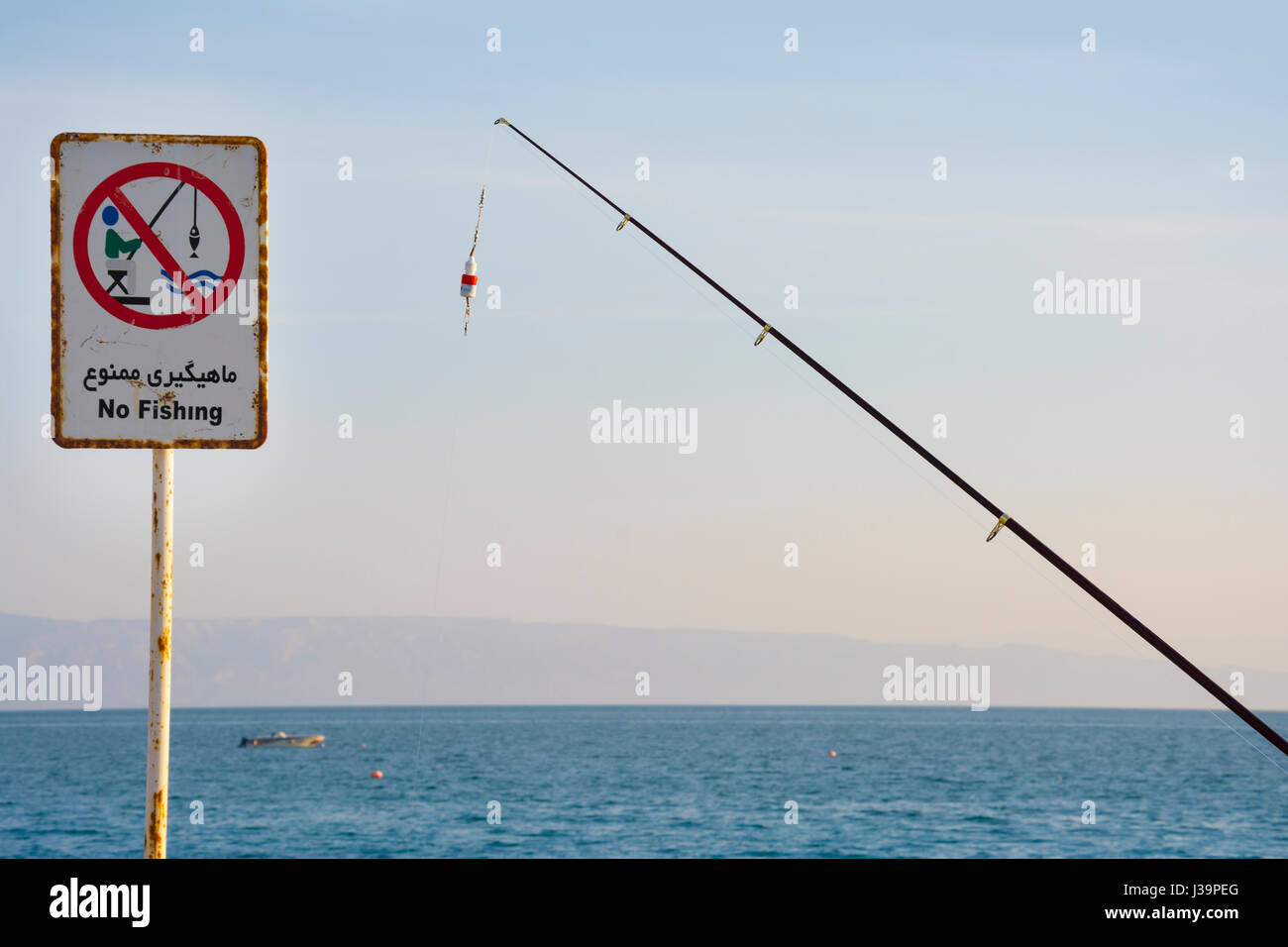 Eine Angelrute neben Zeichens keine Angeln am Pier erklärt Angeln in diesem Gewässer illegal sein. Leute fangen Fische unter einem Schild, das sagt Stockfoto