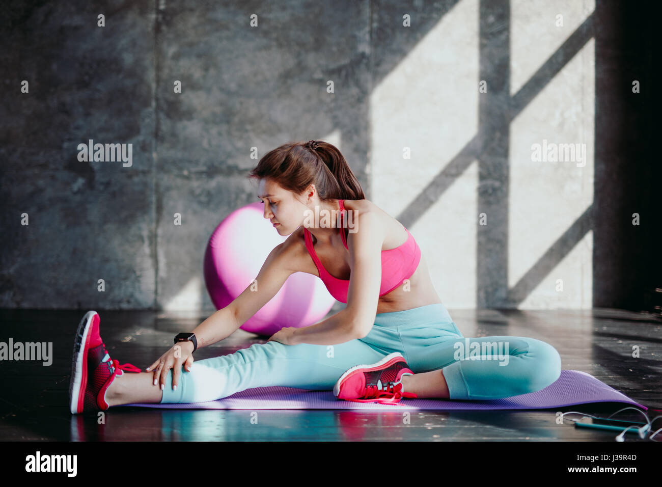 junge Frau stretching Muskelfaserriss im Fitness-Studio, Fit weiblich Warm-up auf lila Matte zu tun. Stockfoto