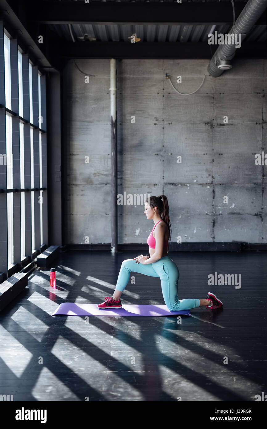 Seite Ansicht Portrait schöne junge Frau trägt weißes Tank-Top trainieren gegen graue Wand, Yoga oder Pilates Übung. Stehend in Krieger Stockfoto