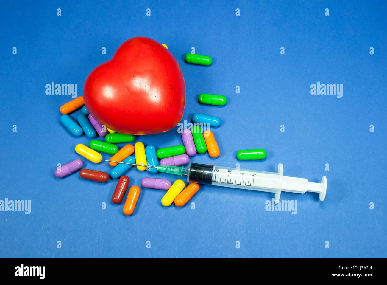 Medizinische Spritze teilweise gefüllt mit Flüssigkeit, horizontal platziert unter einem Haufen von verschiedenen farbigen Pillen mit roten schwammig Herz, medizinisches Konzept Stockfoto