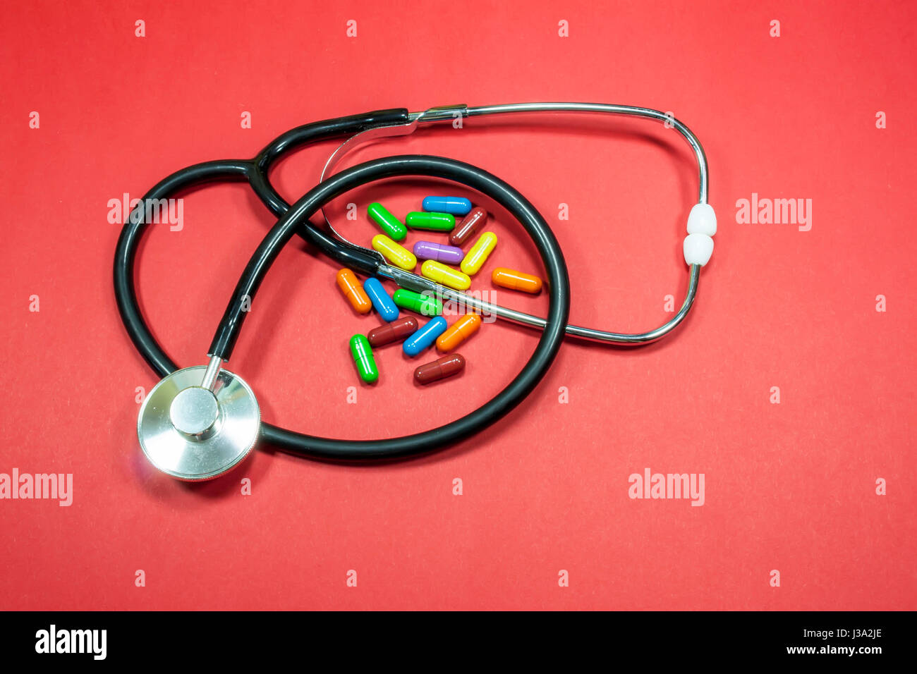 Medizinische Stethoskop und Haufen von farbigen Pillen oder Drogen vor rotem Hintergrund Stockfoto