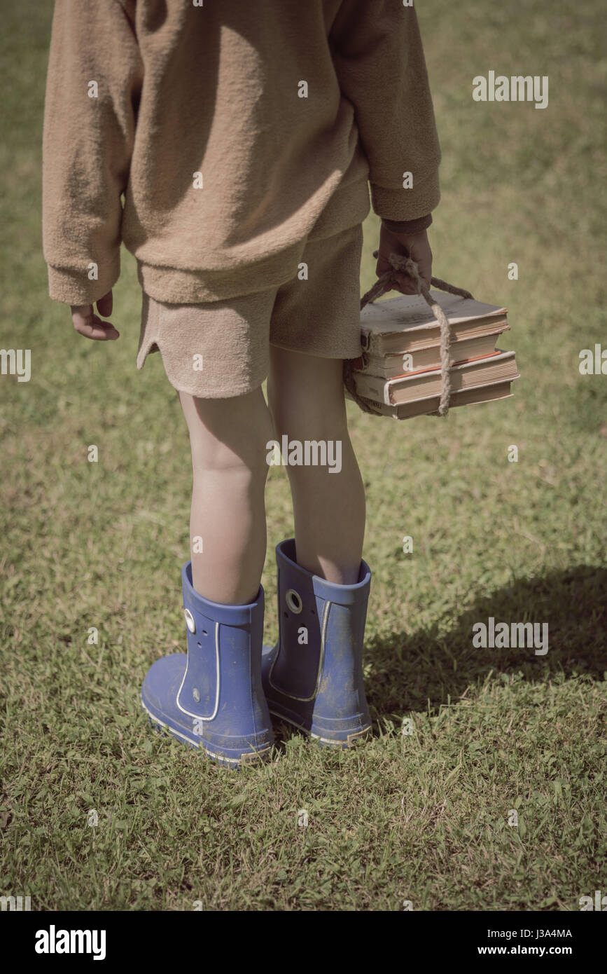 Junge im blauen Gummistiefeln und braune kurze Hosen, Bücher in der hand Stockfoto