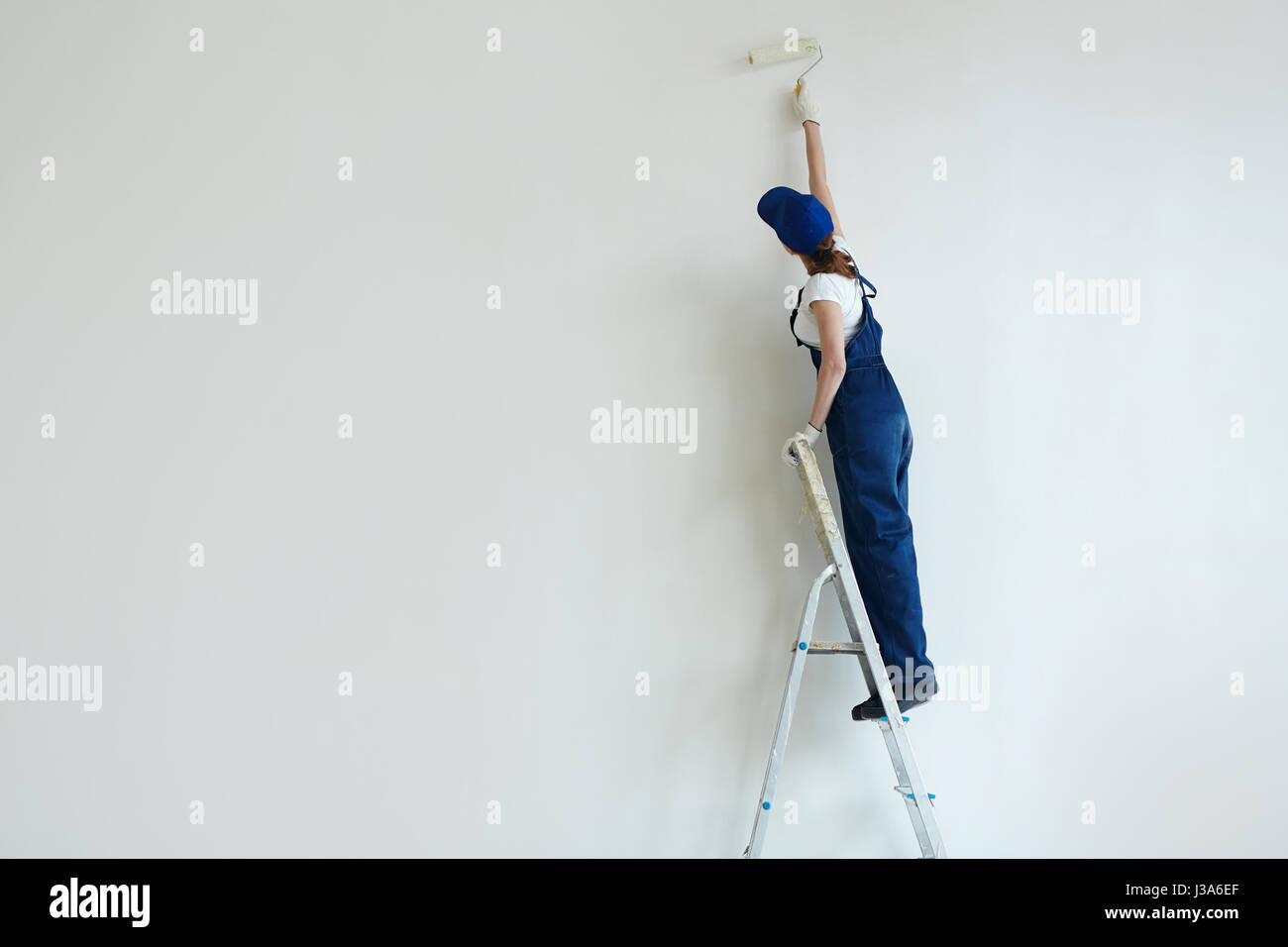 Frau Malerei Wand auf Stehleiter Stockfoto