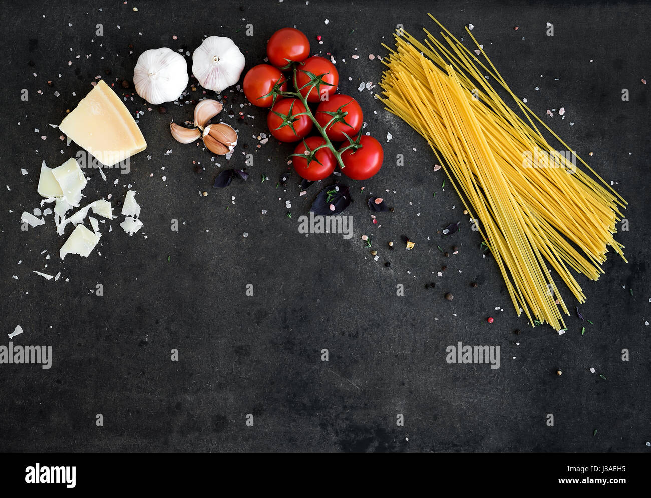 Essen-Frame. Pasta Zutaten. Cherry-Tomaten, Spaghetti Nudeln, Knoblauch, Basilikum, Parmesan und Gewürzen auf dunklen Grunge Hintergrund, Textfreiraum, Horizontal ausgerichtet Stockfoto