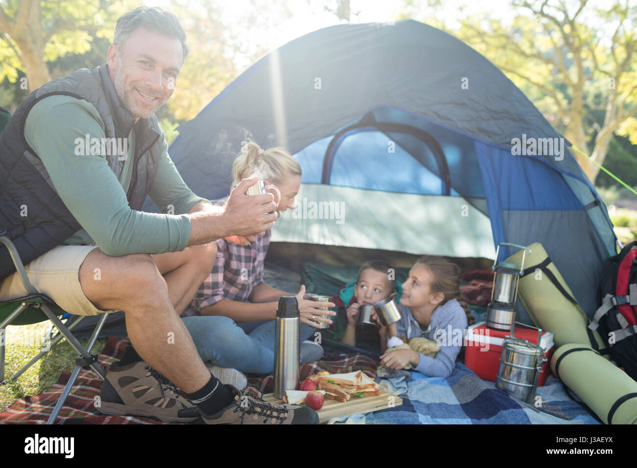 Familie lächelnd mit Snacks und Kaffee außerhalb des Zeltes auf Campingplatz Stockfoto