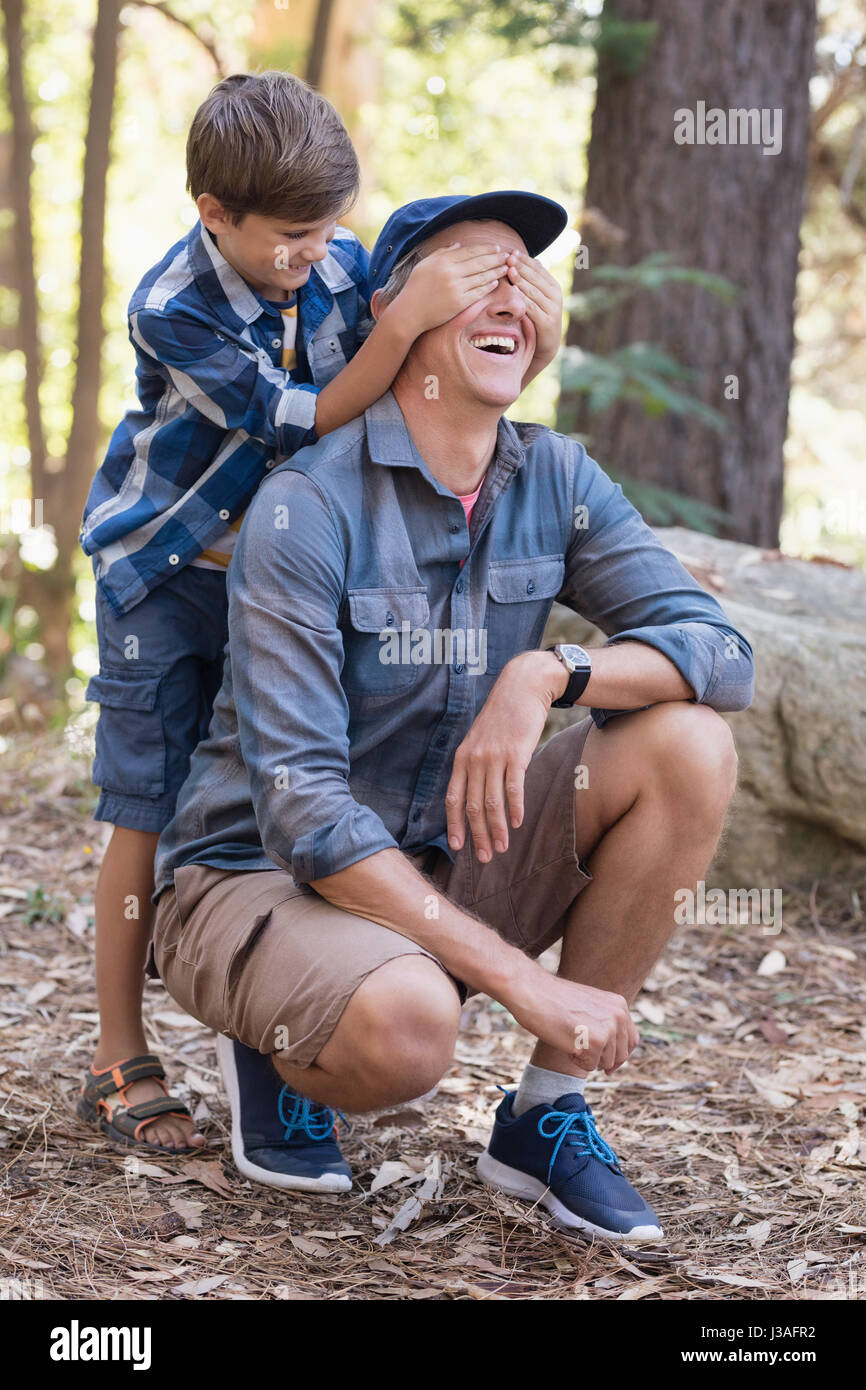 Verspielter kleiner Junge Väter Augen beim Wandern im Wald bedecken Stockfoto