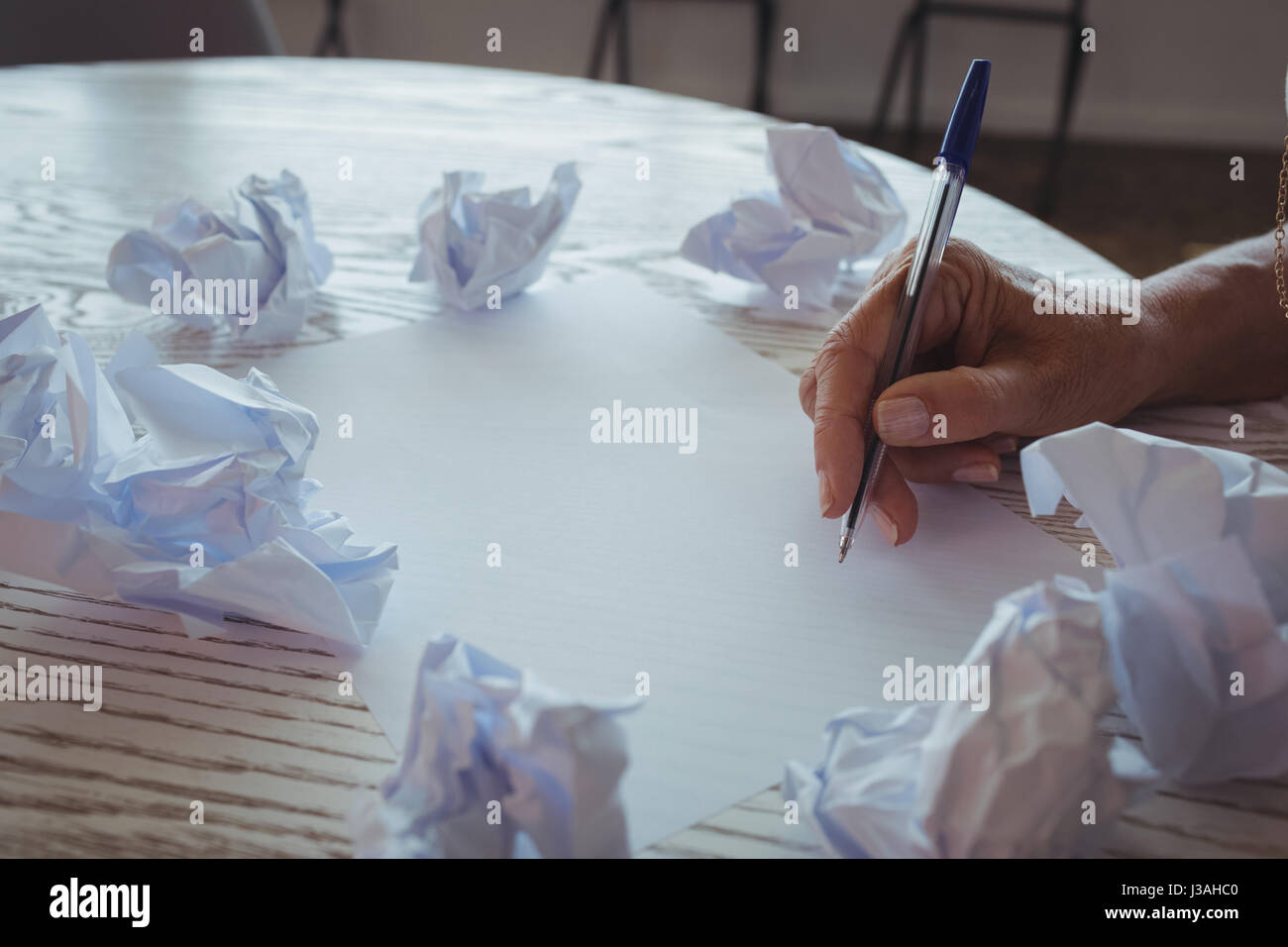 Hand der Geschäftsfrau schreiben inmitten zerknitterten Papiere auf Schreibtisch beschnitten Stockfoto