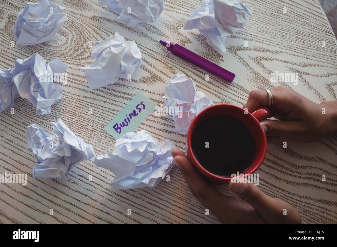 Hand der Geschäftsfrau hält Kaffee von zerknitterten Papiere auf Schreibtisch im Büro beschnitten Stockfoto