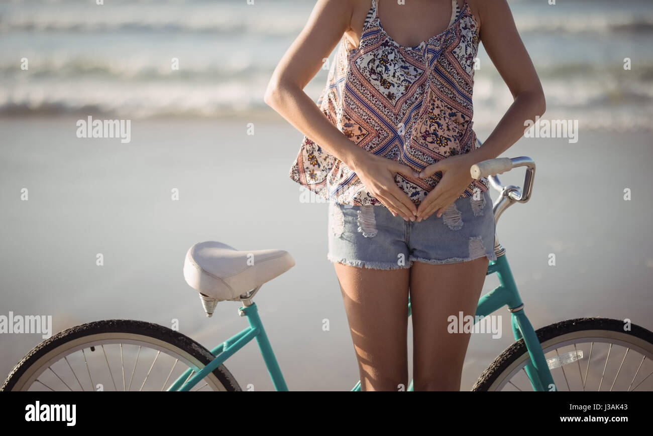 Mittleren Bereich der Frau machen Herzform mit Händen stehend mit dem Fahrrad am Strand Stockfoto