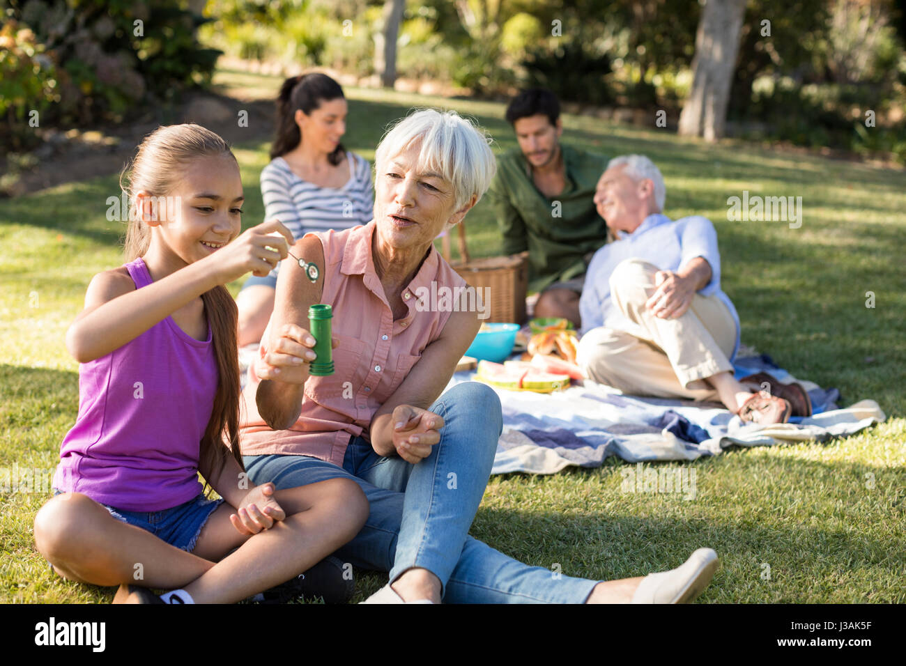 Großmutter ihre Enkelin bläst Seifenblasen im Park an einem sonnigen Tag zu betrachten Stockfoto