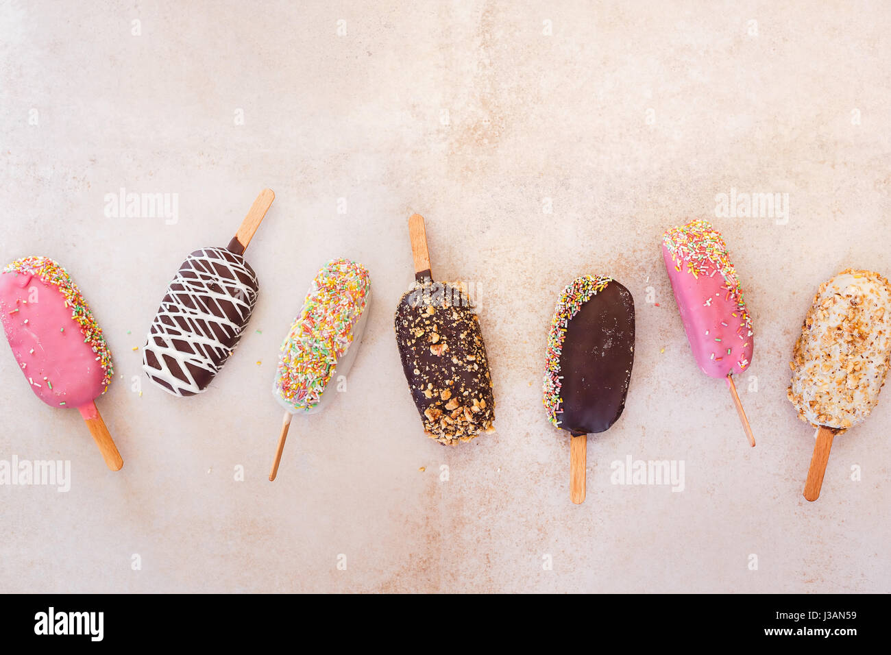 Eis-sticks mit Schokolade, Obst, gerösteten Mandeln und bunten Zucker Streusel auf rustikalen Hintergrund. Ansicht von oben, Leerzeichen Stockfoto