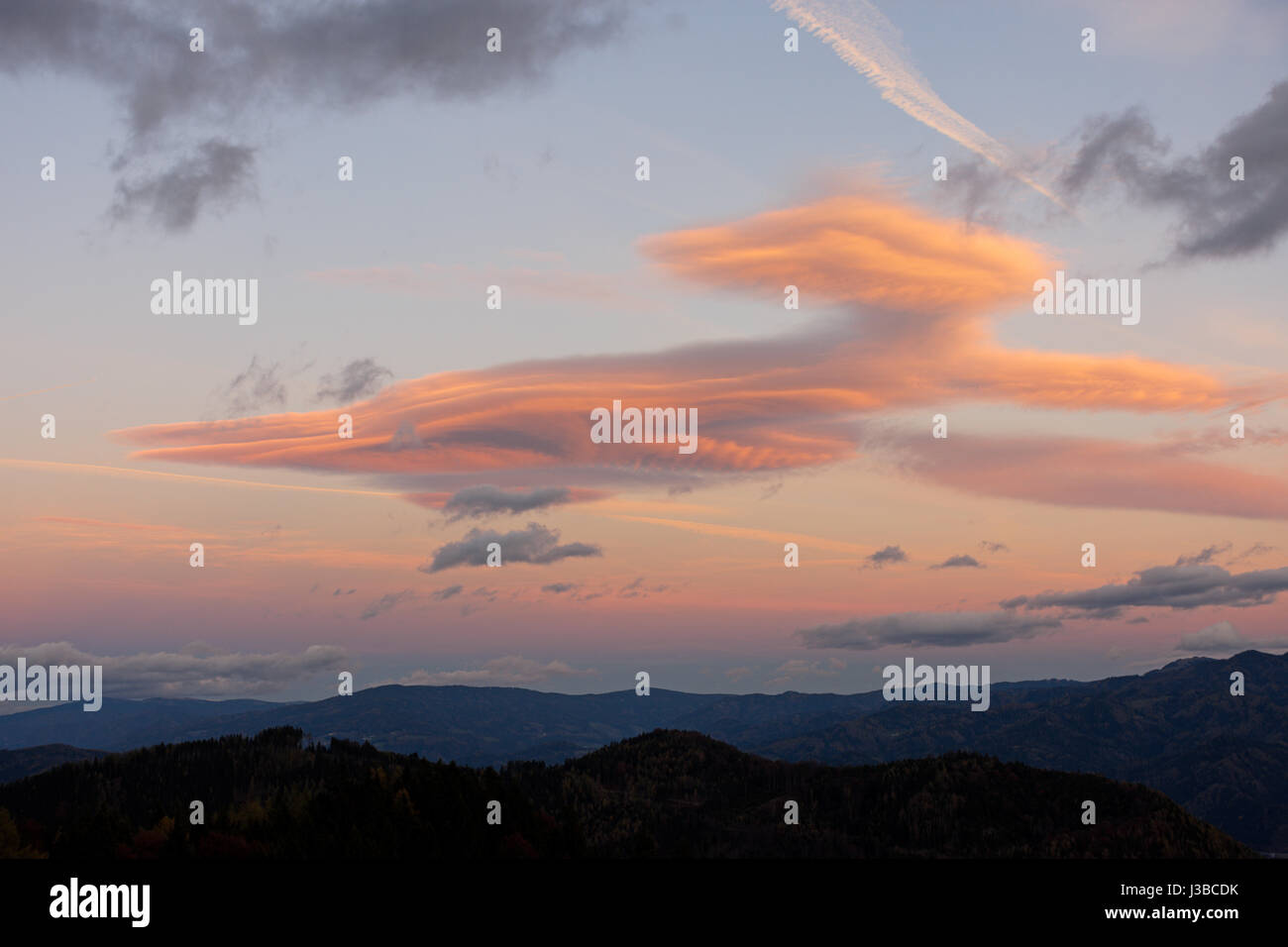 Linsenförmige Wolken beleuchtet von der untergehenden Sonne über eine bergige Landschaft. Steiermark, Österreich. Stockfoto