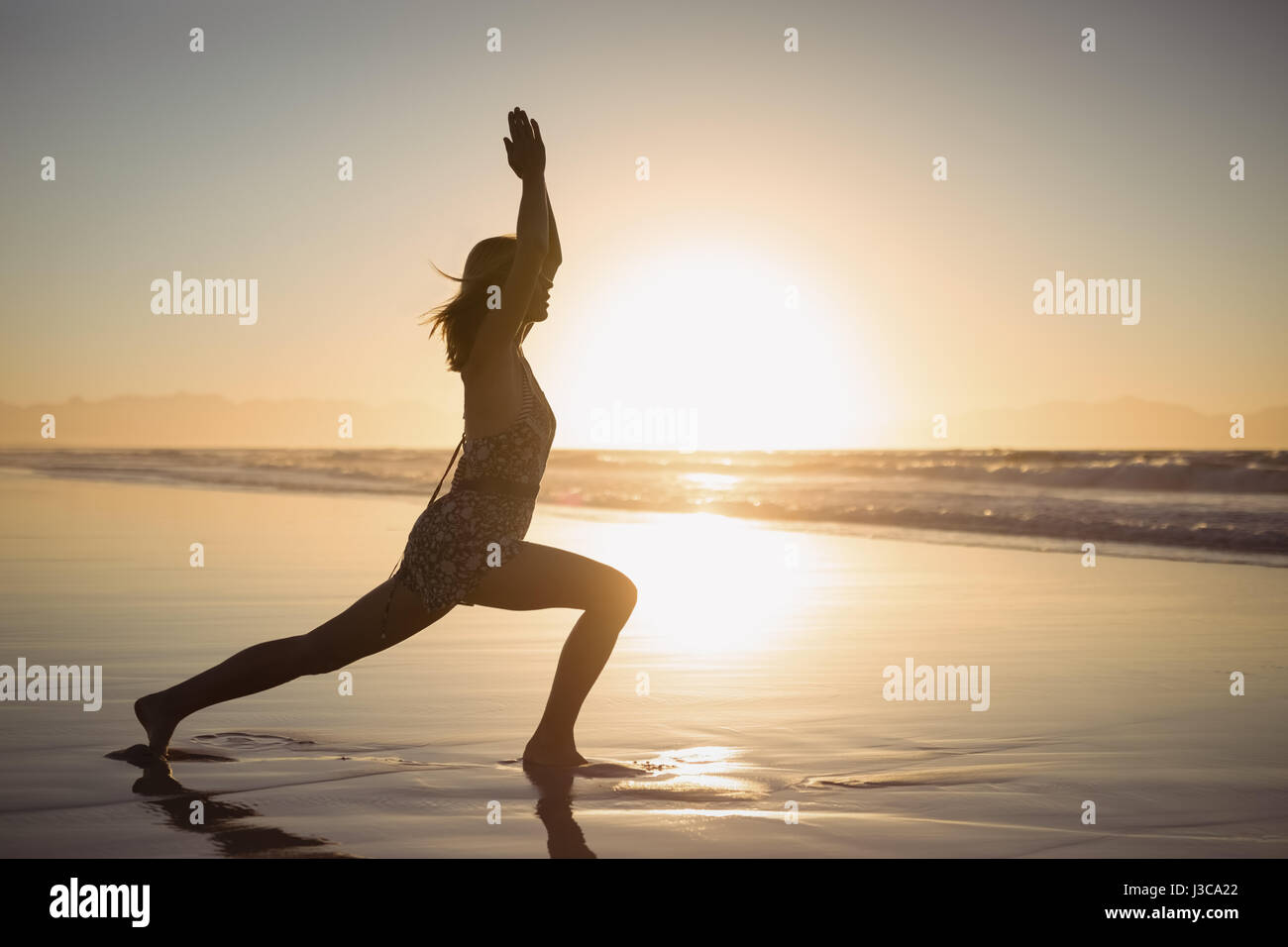 Seitenansicht der Silhouette Frau tun Yoga am Ufer am Strand während der Dämmerung Stockfoto