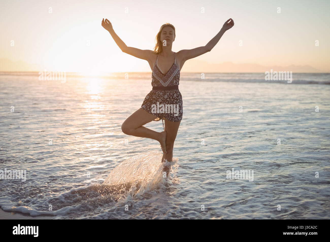 Frau tut Yoga im Meer am Strand während der Dämmerung Stockfoto