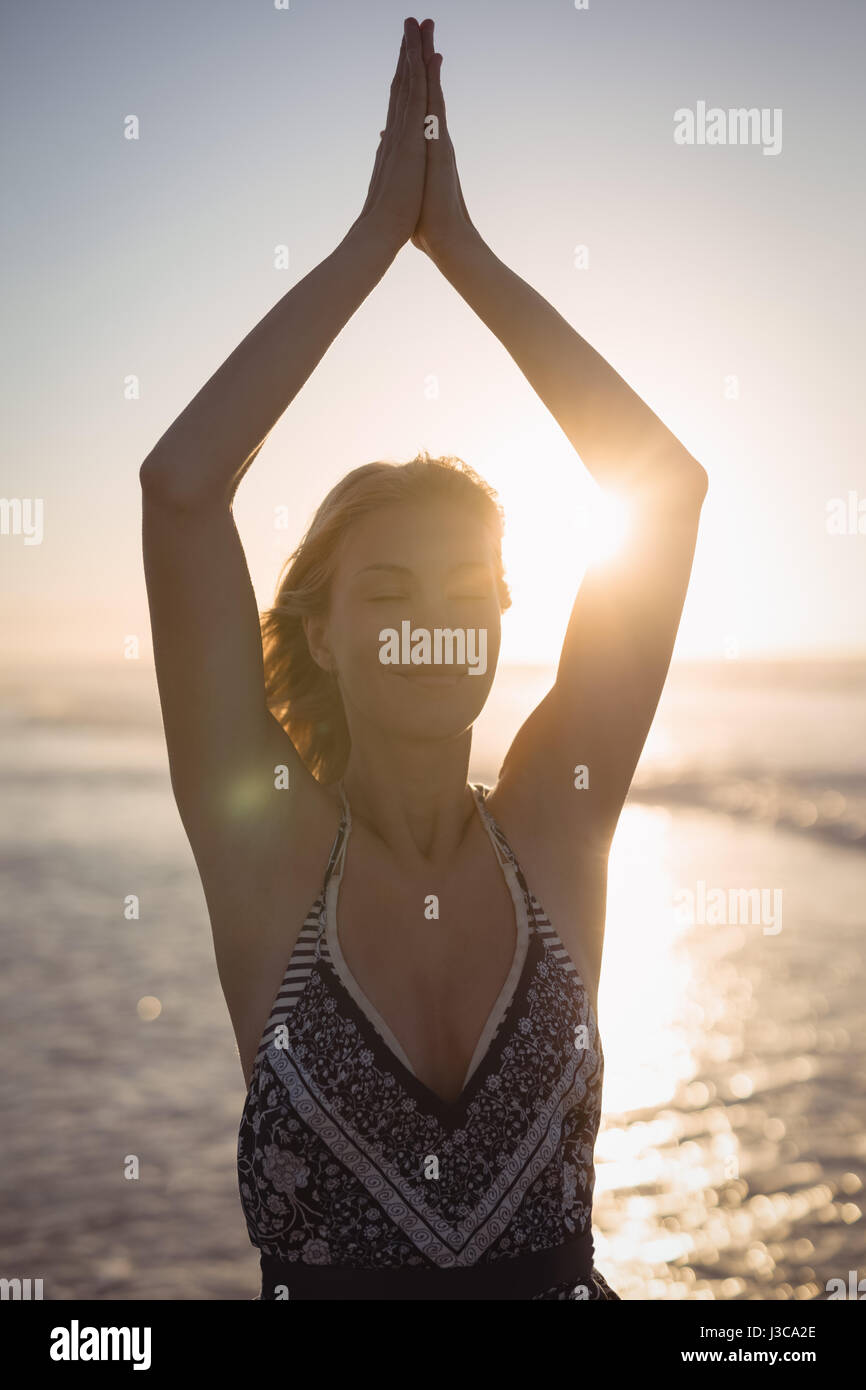 Junge Frau mit erhobenen Armen tun Yoga am Strand während der Dämmerung Stockfoto