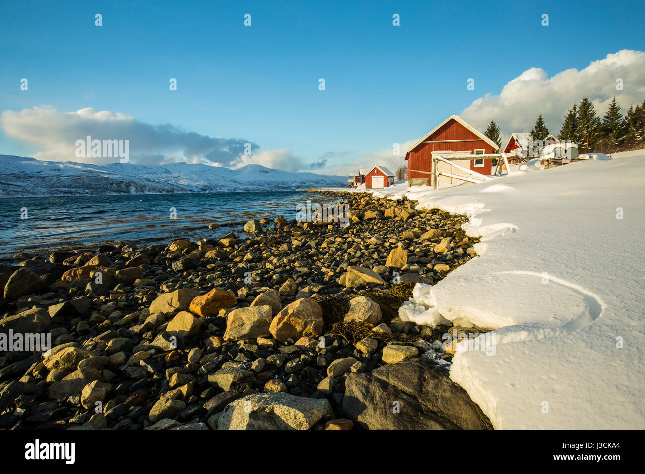 Typische norwegische warme und gemütliche Haus befindet sich am See an einem Fjord in Troms Grafschaft, Norwegen. Die Sonne über dem Horizont niedrig eingestellt ist und der Himmel ist Stockfoto