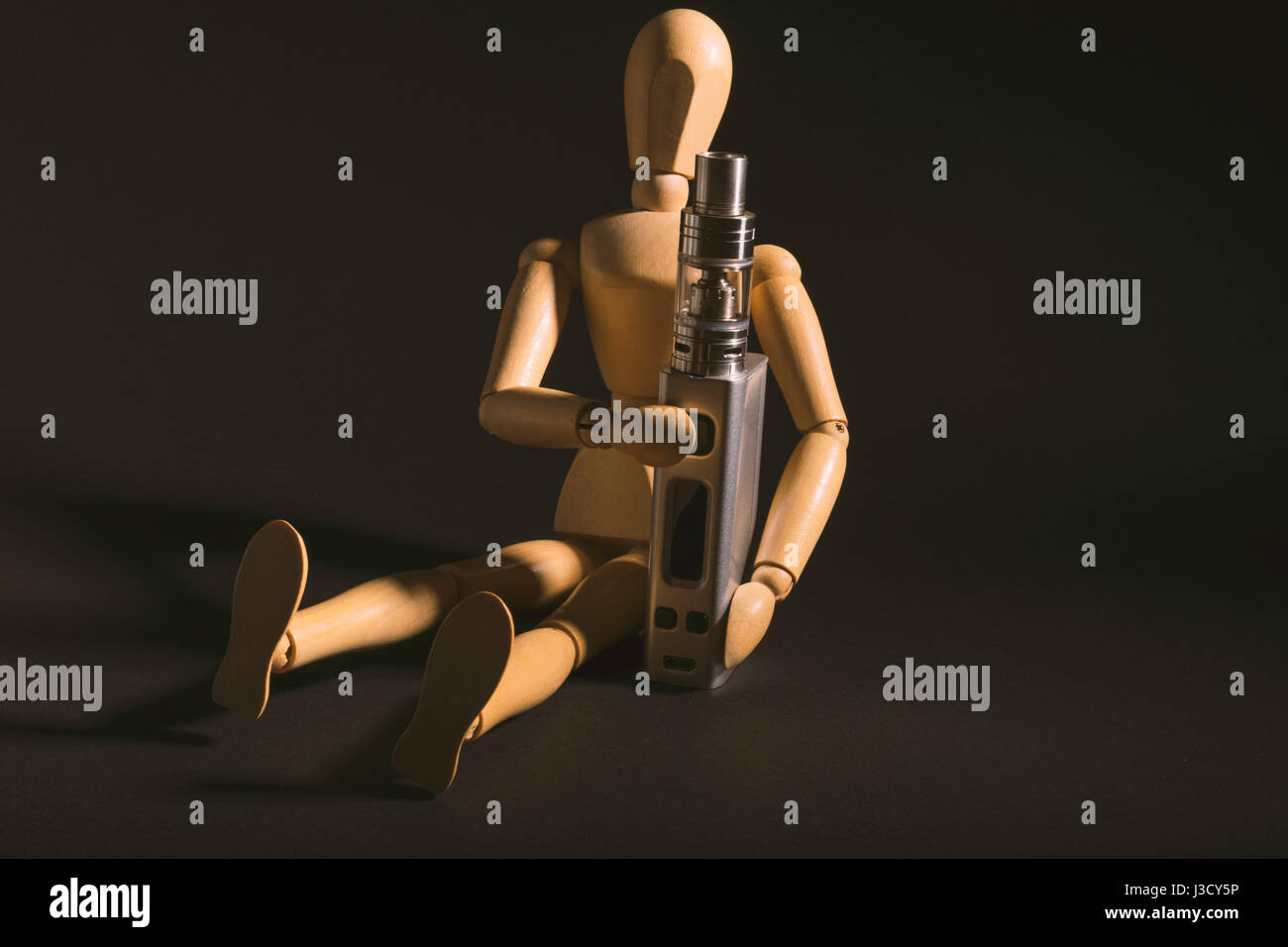 wooden dummy sitzen neben eines elektronischen Zigarette oder Dampfen Geräts isoliert. isoliert auf einem dunklen Hintergrund. Stockfoto