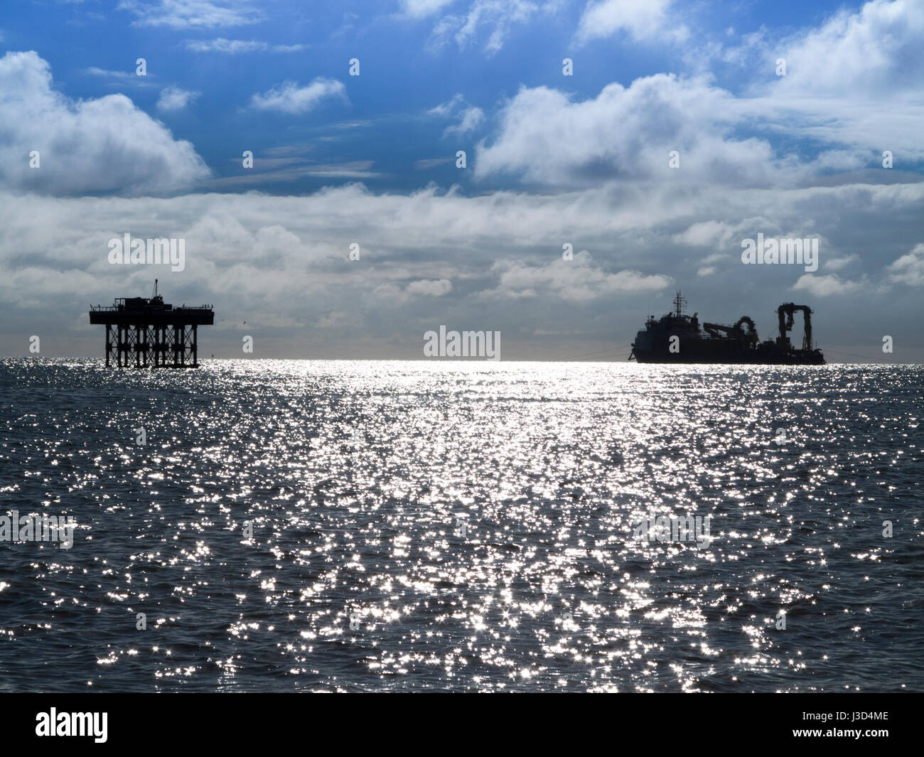 Eine Silhouette Kabelverlegung Schiff auf einen hellen sonnigen Horizont mit schimmernden Meer im Vordergrund Stockfoto