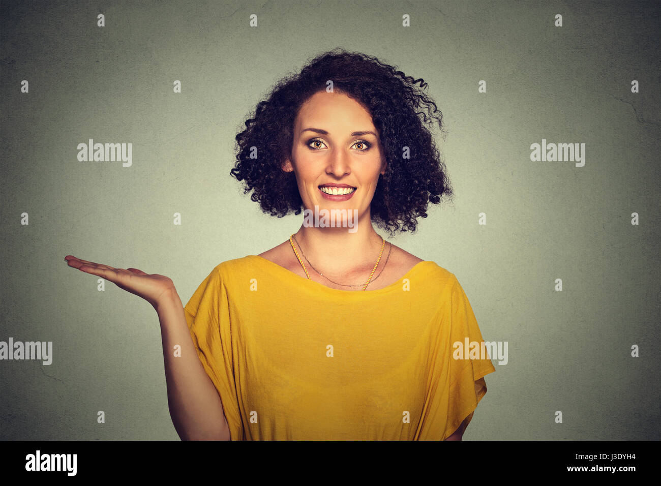 Closeup Portrait glücklich ziemlich zuversichtlich, dass junge lächelnde Frau gestikulieren präsentiert Raum auf der linken Seite mit der Handfläche nach oben isoliert grau hinterlegt. Positiven menschlichen e Stockfoto