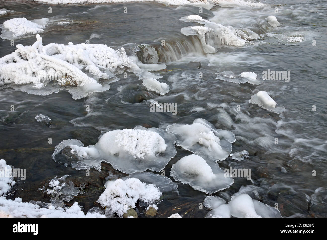 Schäumende Stromschnellen des Flusses, bedeckt mit Wucherungen von Eis und Büsche Trockenrasen in Rauhreif Kristalle am Ufer an einem Winterabend Stockfoto