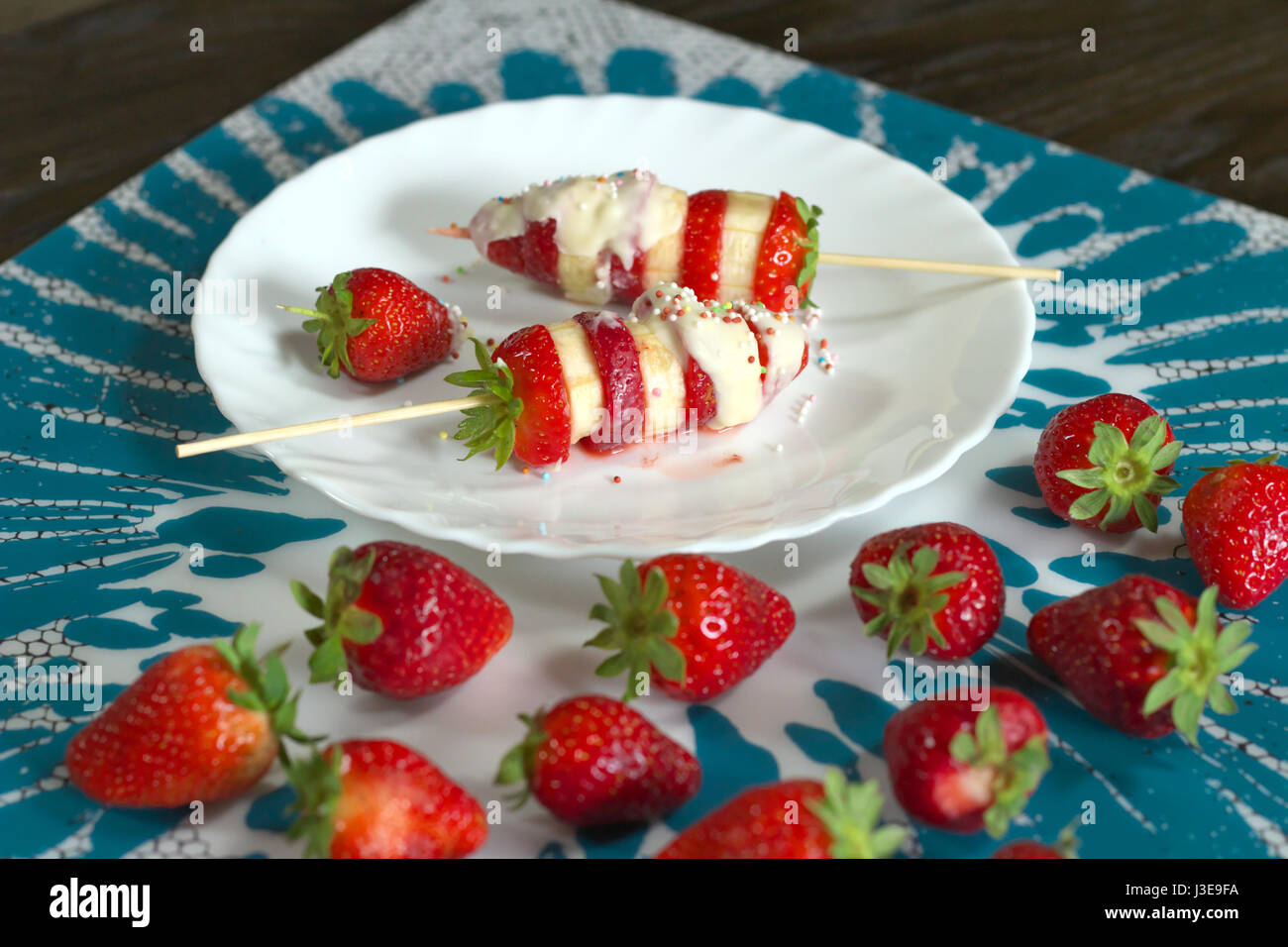 Erdbeere und Banane Spieße vorbereitet Rezept mit weißer Schokolade und bunten Zucker Dekorationen - rote Erdbeeren im Vordergrund servierbereit Stockfoto