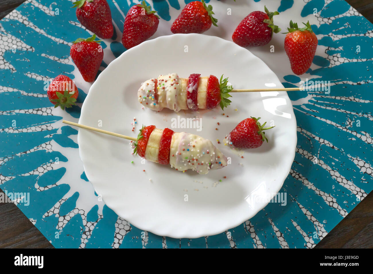 Erdbeere und Banane Spieße vorbereitet Rezept servierfertig mit weißer Schokolade und bunten Zucker Dekorationen - direkt über Ansicht Stockfoto