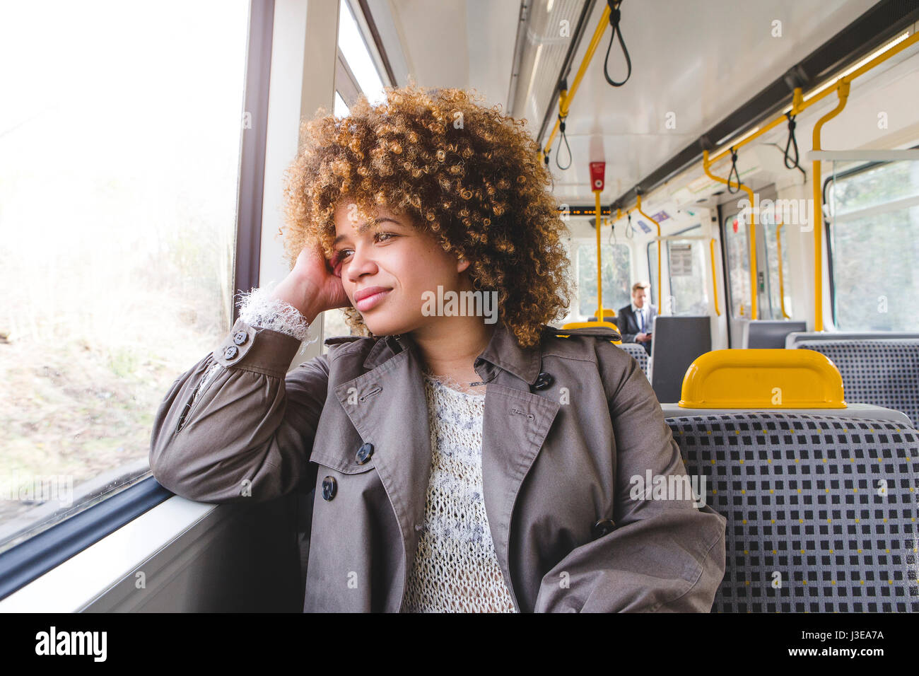 Frau sitzt in einem Zug. Sie hat ihren Ellenbogen auf dem Fenstersims und ruht sich ihr Kopf auf ihre Hand, schaut aus dem Fenster. Stockfoto
