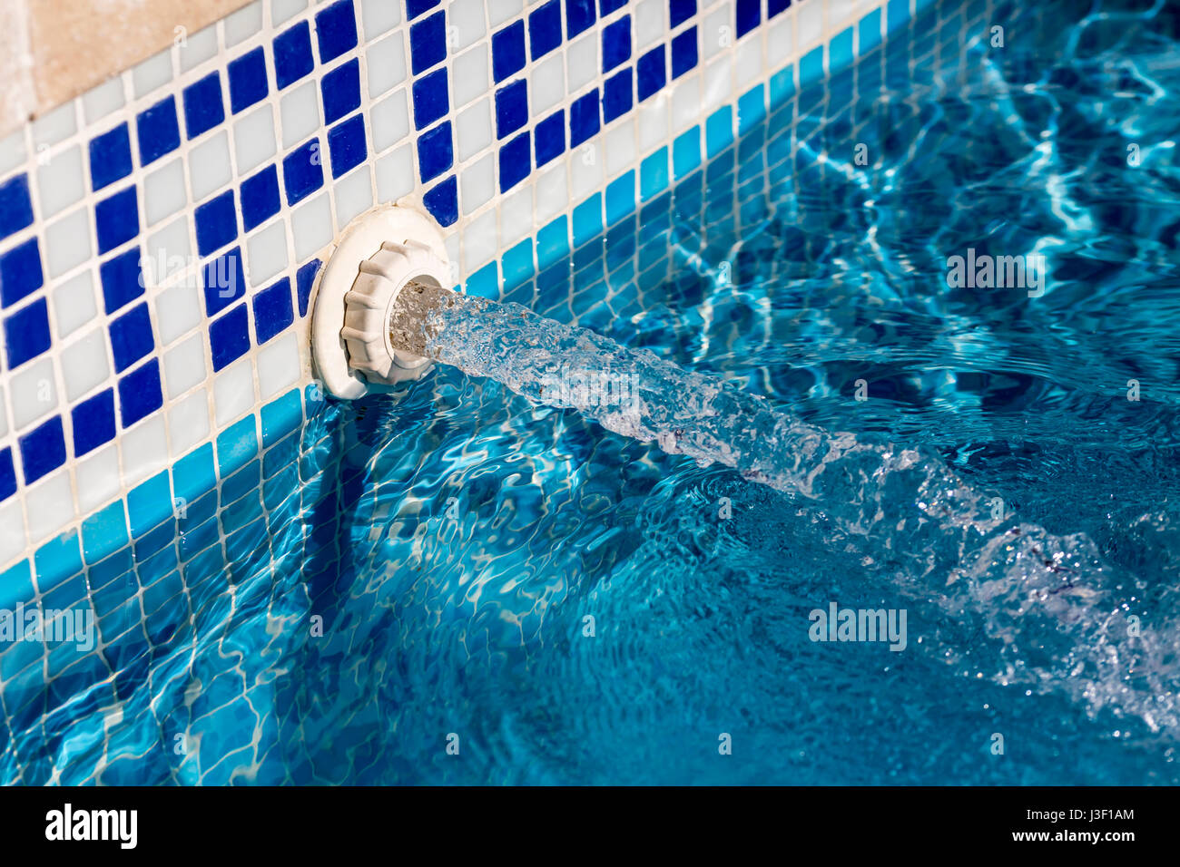 Detailansicht eines einströmende Wasser-Jets in ein Schwimmbecken mit blauen Kacheln Stockfoto