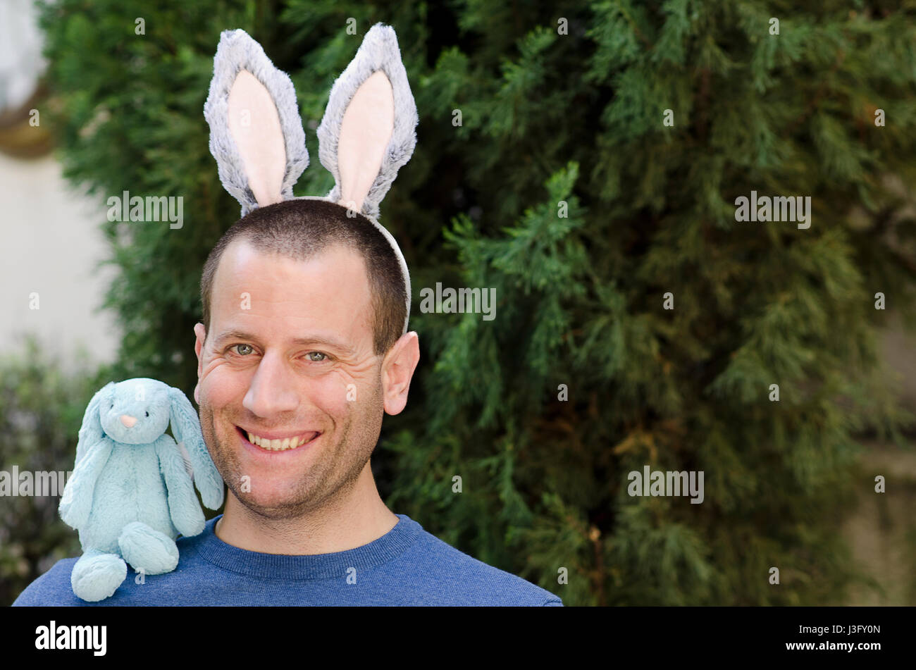 Das Osterfest! Mann mit Hasenohren und ein Hase Stofftier auf seiner Schulter. Stockfoto