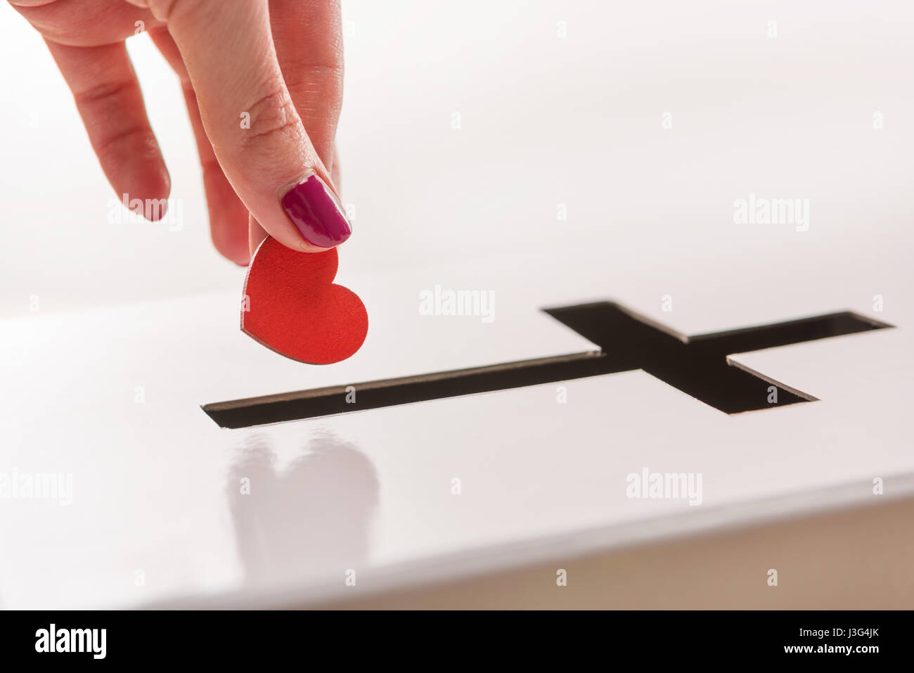 Close-up Teilansicht des Woman einfügen Rot Herz Symbol in Loch für Spenden in Form eines Kreuzes, Spende und Glaubens-Konzept Stockfoto